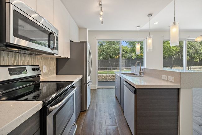 Kitchen featuring stainless steel appliances, a kitchen island with sink, modern cabinets, dark wood finished floors, and pendant lighting | Image 9