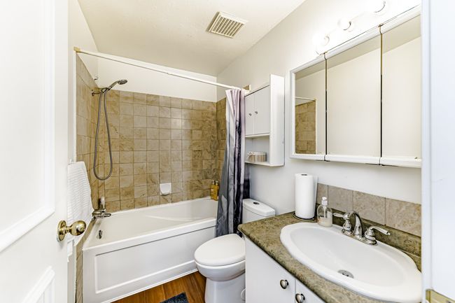 Bathroom with visible vents, toilet, shower / bath combo with shower curtain, wood finished floors, and vanity | Image 9