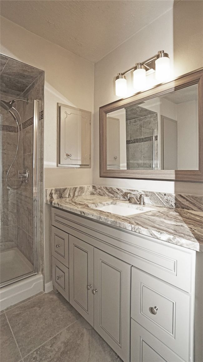 The primary bathroom features a good sized vanity with a nice mirror, gorgeous granite counters, nice lighting, lots of cabinet/drawer space, a medicine cabinet, and a walk in shower | Image 15