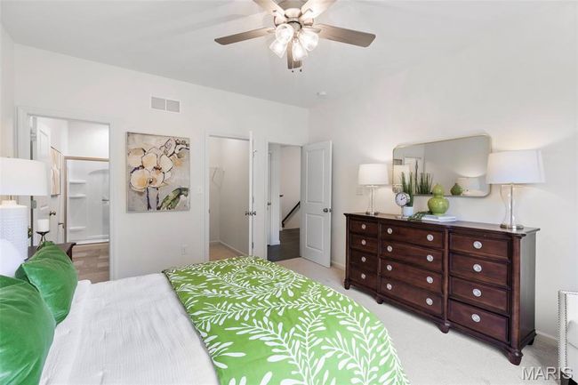 Bedroom with a walk in closet, light colored carpet, ensuite bath, baseboards, and ceiling fan | Image 20