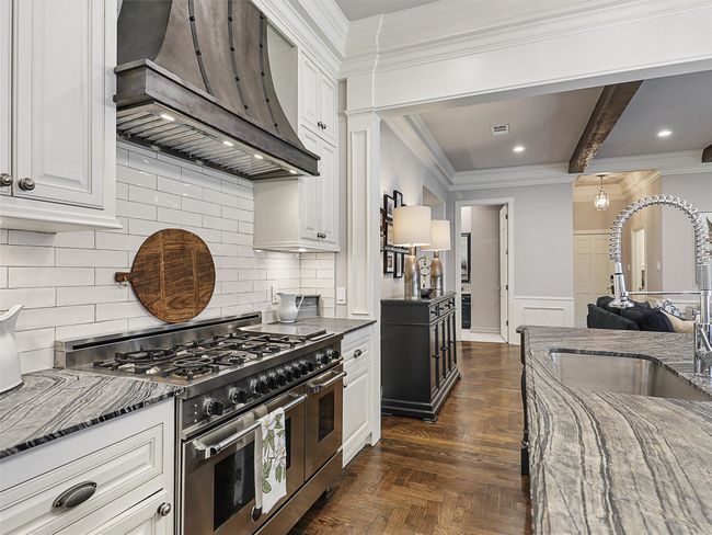 Kitchen with double oven range, wall chimney exhaust hood, dark stone counters, white cabinets, and wainscoting | Image 14