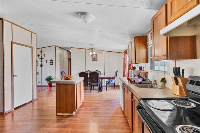Kitchen featuring a center island, brown cabinets, white microwave, stainless steel range with electric cooktop, and under cabinet range hood | Image 11