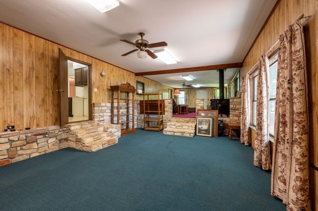 Unfurnished living room with a wood stove, a ceiling fan, wooden walls, and carpet | Image 22