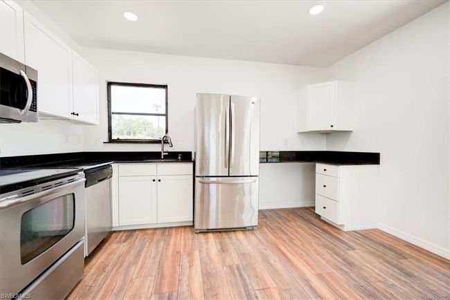 Kitchen with white cabinets, a sink, appliances with stainless steel finishes, light wood-style floors, and dark countertops | Image 32