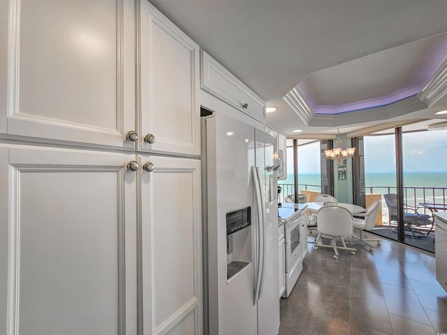 Kitchen featuring white appliances, a chandelier, white cabinetry, a tray ceiling, and a water view | Image 18