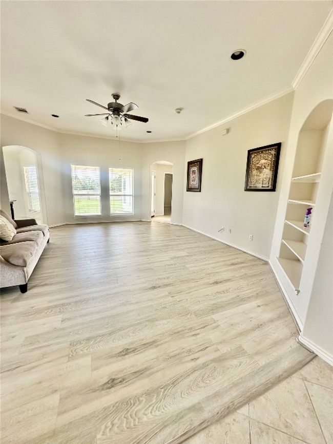 Unfurnished living room with arched walkways, ceiling fan, crown molding, built in shelves, and light wood-style floors | Image 7