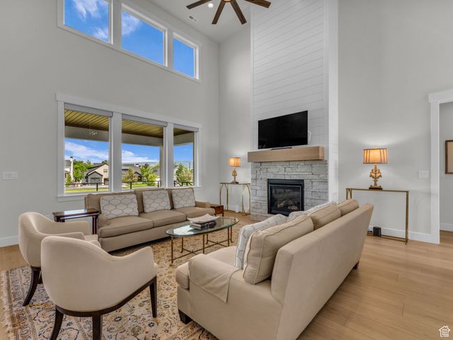 Living room with a high ceiling, a ceiling fan, a fireplace, baseboards, and light wood-type flooring | Image 12