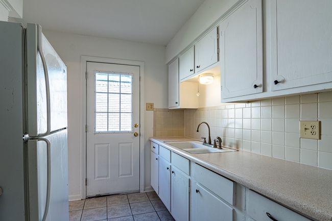 1214 Hunt - Kitchen featuring light countertops, a sink, backsplash, light tile patterned floors, and freestanding refrigerator | Image 8