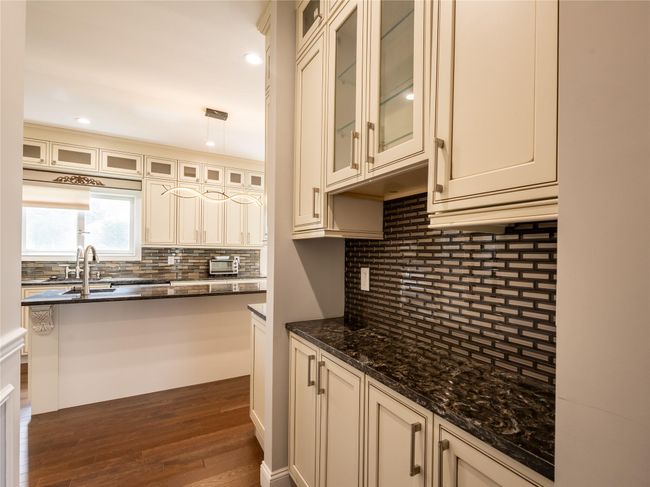 Kitchen with a sink, dark stone counters, decorative backsplash, cream cabinetry, and dark wood-type flooring | Image 11