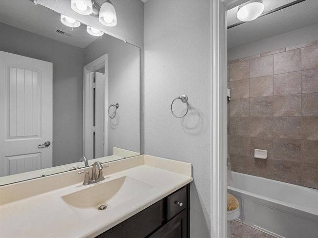 This bathroom features a modern vanity with a sleek sink, large mirror, and overhead lighting. The room includes a tiled bathtub and shower combination, complemented by neutral wall colors for a clean and fresh look. | Image 31