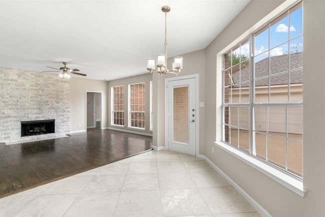 Unfurnished living room with baseboards, tile patterned floors, ceiling fan with notable chandelier, and a stone fireplace | Image 15
