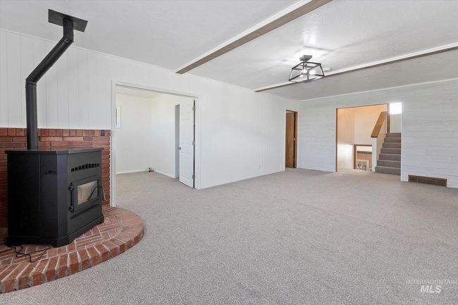 Unfurnished living room with a wood stove, carpet floors, stairway, and wood walls | Image 9