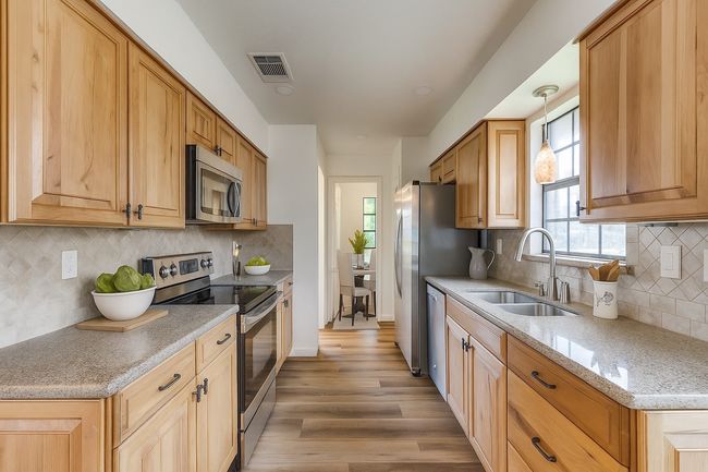 Kitchen with stainless steel appliances, light wood finished floors, decorative backsplash, light stone counters, and hanging light fixtures | Image 4