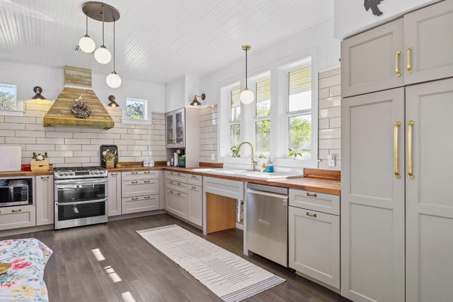 Kitchen with wooden counters, appliances with stainless steel finishes, wall chimney range hood, backsplash, and hanging light fixtures | Image 12