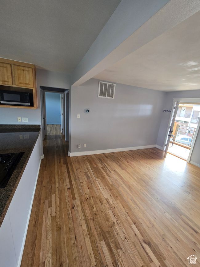 Kitchen with light wood finished floors, dark countertops, light brown cabinets, black gas cooktop, and open floor plan | Image 14