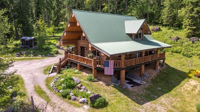 Back of house with a wooded view, log exterior, metal roof, dirt driveway, and a wooden deck | Image 70