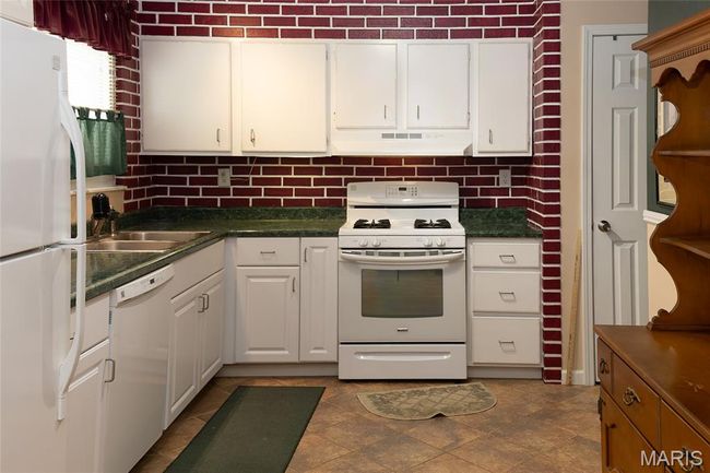 Kitchen featuring white appliances, under cabinet range hood, dark countertops, decorative backsplash, and white cabinets | Image 8