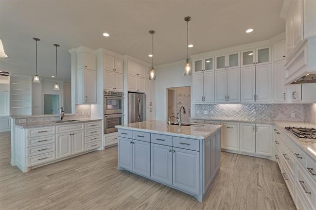 The kitchen island showcases a soft blue finish that pairs beautifully with the Cambria quartz countertops, creating a cohesive and stylish focal point. Designed with functionality in mind, the island offers storage on both sides for added convenience. The prep sink at the peninsula is complemented by custom wine cabinets, with the option to install a wine refrigerator, if desired. | Image 15
