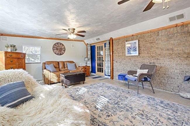 Tiled living room featuring ceiling fan, ornamental molding, a textured ceiling, and brick wall | Image 14