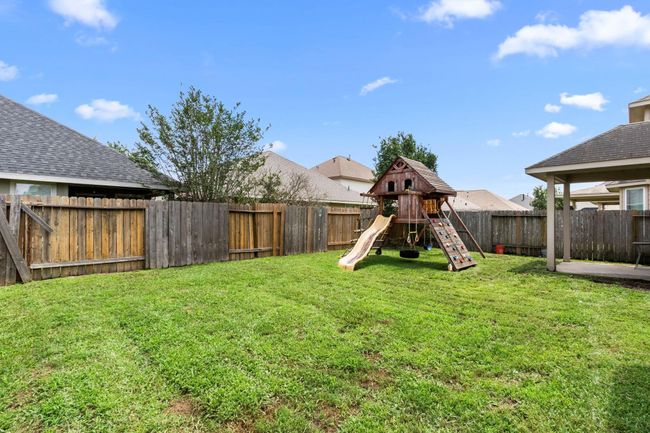 Spacious backyard with a well-maintained lawn, featuring a wooden playset for kids. The area is enclosed with a wooden fence, offering privacy and a safe play environment. Ideal for family activities and outdoor enjoyment. | Image 31