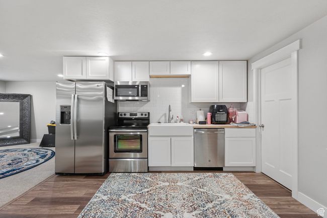 Kitchen featuring appliances with stainless steel finishes, backsplash, white cabinetry, wood finished floors, and recessed lighting | Image 26