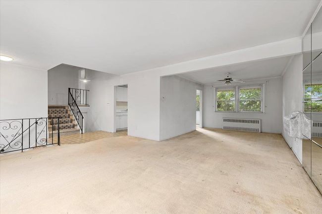 Unfurnished living room featuring radiator, light colored carpet, ceiling fan, and stairs | Image 5