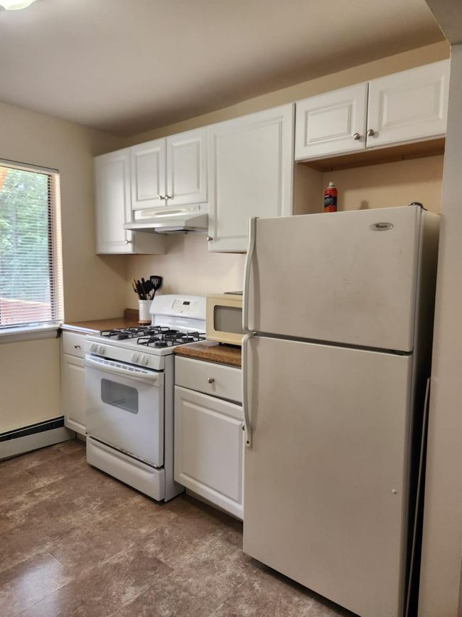 Kitchen with white appliances, under cabinet range hood, white cabinets, and baseboard heating | Image 6
