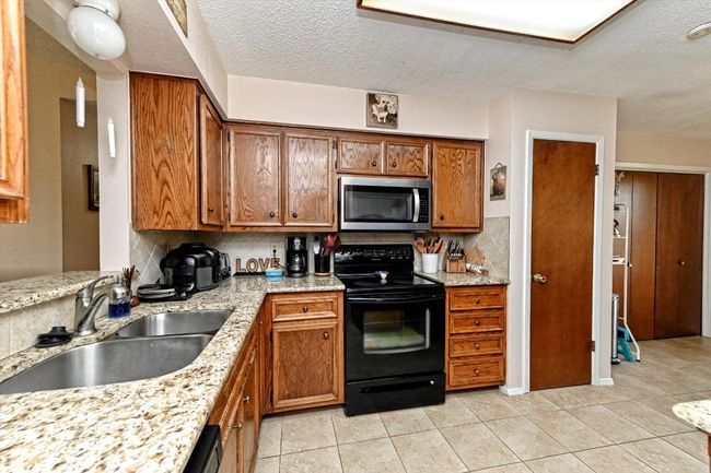 Kitchen featuring black electric range oven, stainless steel microwave, backsplash, a stainless steel sink, and brown cabinetry | Image 9