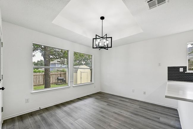 Unfurnished dining area with healthy amount of natural light, wood finished floors, a raised ceiling, and a chandelier | Image 15