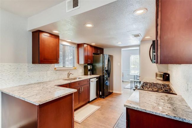 Kitchen featuring appliances with stainless steel finishes, a sink, backsplash, light wood-style flooring, and light stone countertops | Image 10