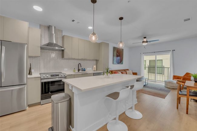 Kitchen with stainless steel appliances, open floor plan, wall chimney range hood, light countertops, and light wood-style flooring | Image 13