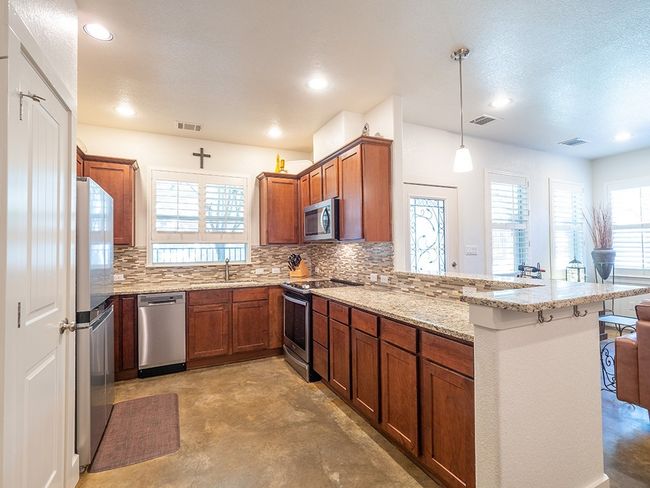 Kitchen with light stone countertops, appliances with stainless steel finishes, brown cabinets, decorative light fixtures, and backsplash | Image 6