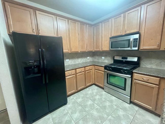 Kitchen with stainless steel appliances, decorative backsplash, light tile patterned floors, and dark stone countertops | Image 7