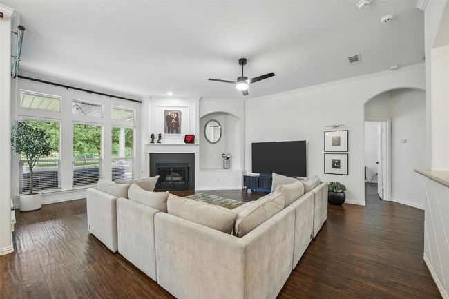 Living area with arched walkways, a fireplace, dark wood-type flooring, a ceiling fan, and crown molding | Image 16