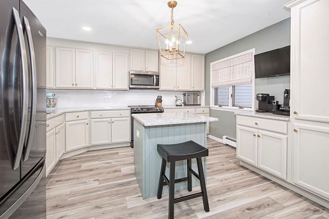Kitchen with backsplash, stainless steel appliances, light wood finished floors, baseboard heating, and a chandelier | Image 11