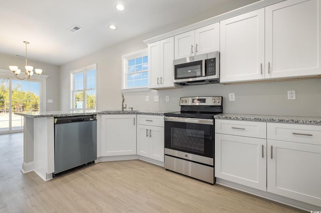 Kitchen featuring appliances with stainless steel finishes, sink, an inviting chandelier, light hardwood / wood-style floors, and white cabinetry | Image 12