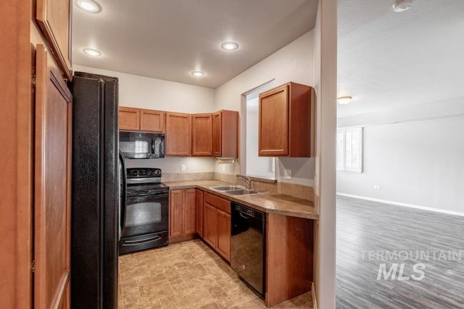 Kitchen with black appliances, brown cabinets, light countertops, recessed lighting, and stone finish floors | Image 8