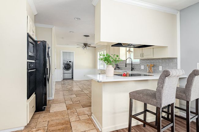 Kitchen featuring washer / dryer, a peninsula, black appliances, crown molding, and light countertops | Image 25