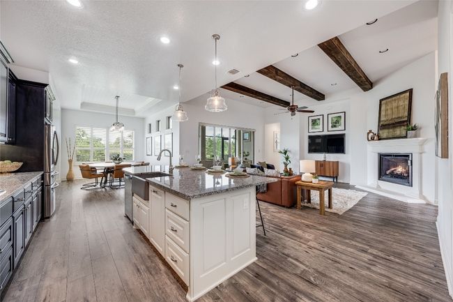 Kitchen with dark wood-style flooring, a glass covered fireplace, a kitchen island with sink, light stone countertops, and recessed lighting | Image 40