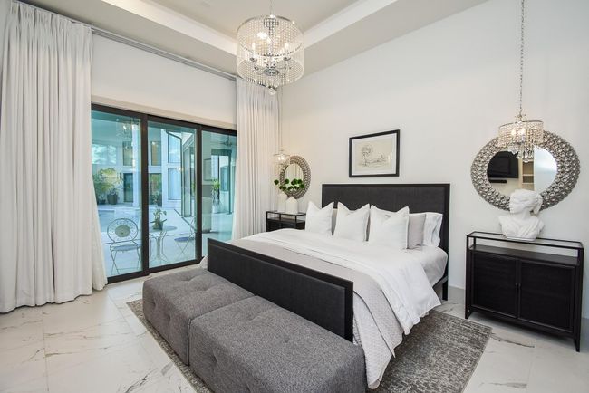 This elegant bedroom features a spacious layout with a modern design with large glass doors leading to an outdoor area, allowing plenty of natural light. The room is accented by luxurious chandeliers and a neutral color palette plus ensuite bathroom. | Image 36