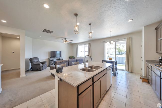 Kitchen featuring stainless steel dishwasher, a sink, a kitchen island with sink, light colored carpet, and light stone countertops | Image 6