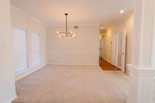 Empty room with ornamental molding, a chandelier, light carpet, and recessed lighting | Image 5