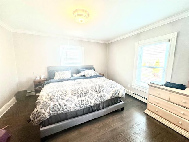 Bedroom with a baseboard heating unit, baseboards, baseboard heating, dark wood-type flooring, and ornamental molding | Image 9
