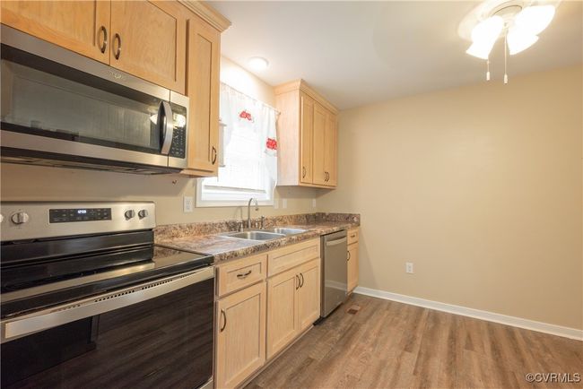 Kitchen featuring stainless steel appliances, light brown cabinetry, baseboards, a sink, and wood finished floors | Image 13