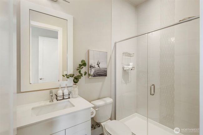 This en suite bath attached to the main-level guest bedroom offers sleek, modern finishes with a glass-enclosed shower, stylish tile detail, and a quartz-topped vanity. Thoughtfully designed for both comfort and elegance, it provides a private and polished space for guests | Image 24