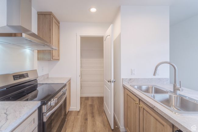 Kitchen with electric range, light brown cabinets, a sink, light wood-style floors, and wall chimney exhaust hood | Image 5