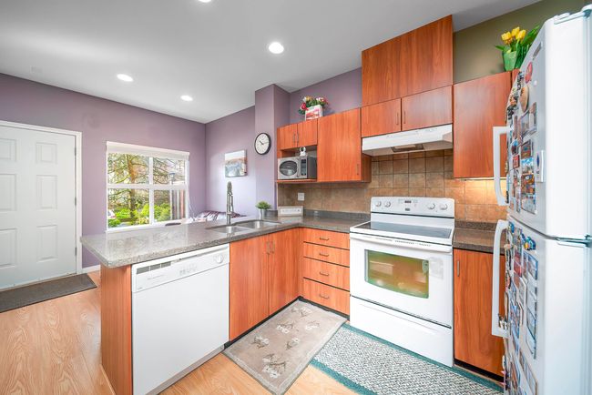 Kitchen featuring under cabinet range hood, a sink, white appliances, a peninsula, and tasteful backsplash | Image 19