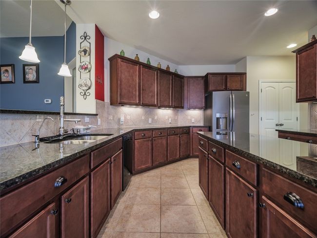 Kitchen with stainless steel fridge with ice dispenser, a sink, black dishwasher, backsplash, and dark stone countertops | Image 19