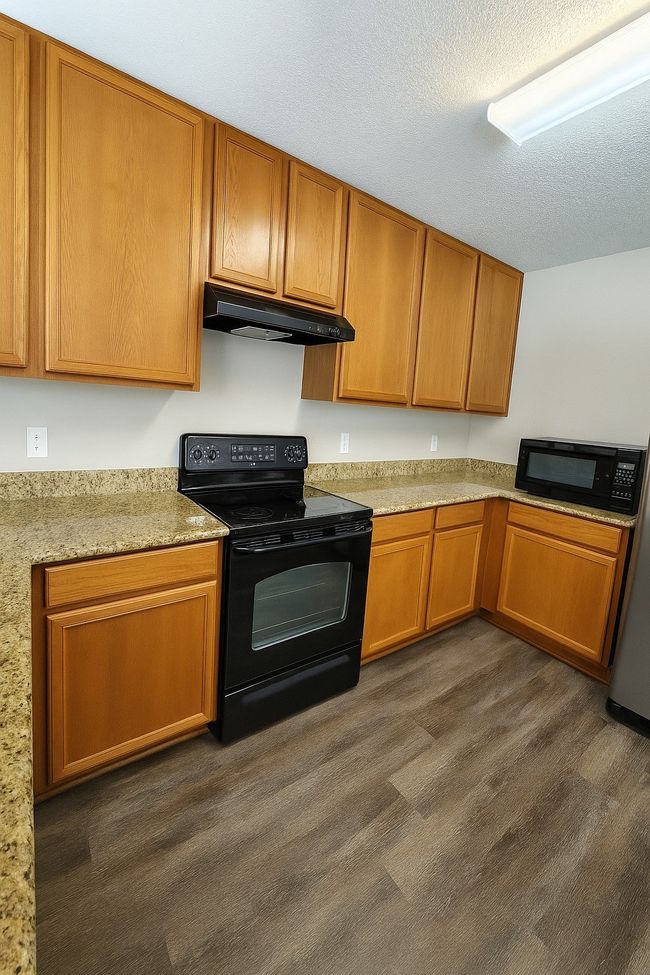 Kitchen featuring black appliances, under cabinet range hood, brown cabinetry, dark wood-type flooring, and a textured ceiling | Image 20