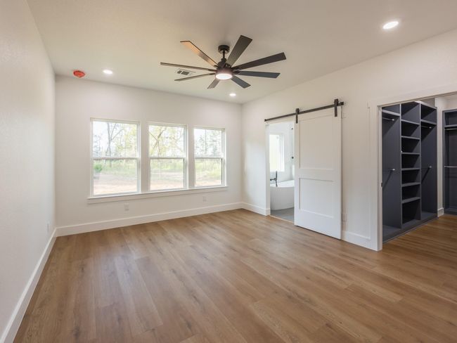 Wake up to peaceful views through triple windows in this spacious primary suite, complete with luxury vinyl plank flooring and a modern ceiling fan for added comfort. | Image 20